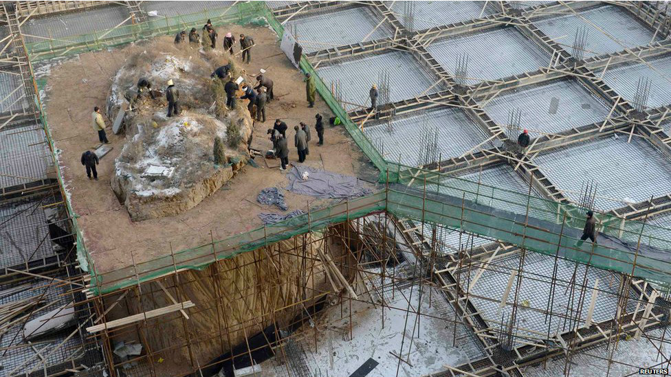 चीन के तियुआन में एक इमारत बनाई जा रही है जिसके बीचोंबीच एक मकबरा था जिसे हटाया जा रहा है.